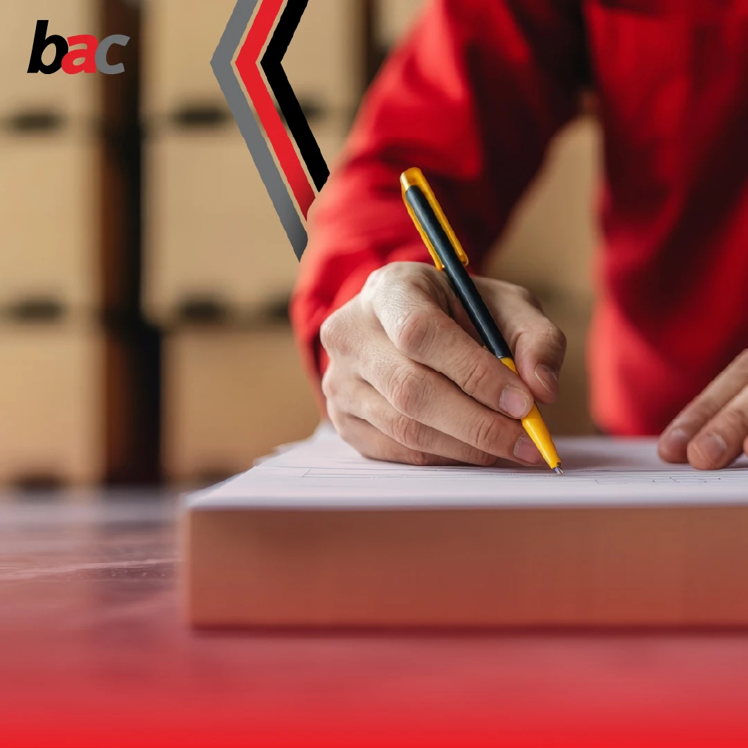 Close-up of hands completing shipping paperwork in a warehouse, BAC branding